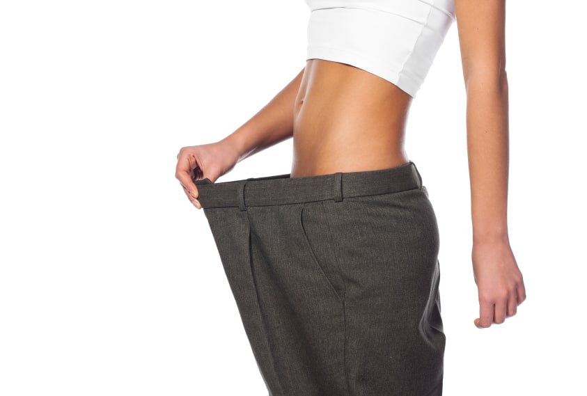 skinny woman in large pant holding them out from her waist to show weight loss