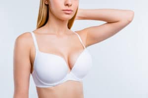 Cropped close-up portrait of nice calm confident attractive lovely blonde, girl chest after uplift injection wearing bra touching hair isolated over light gray background