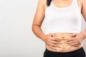 Woman holding her belly after pregnancy, in need of a mommy makeover to boost her confidence